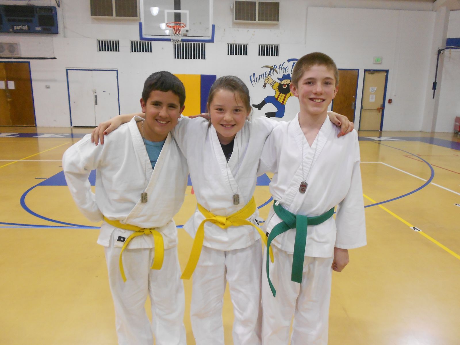 Three young students with yellow and green belts, arms around each other